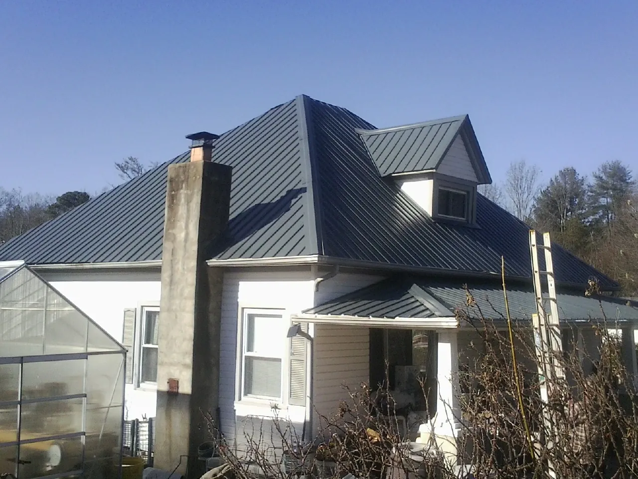Dark blue standing seam metal roof on a white farmhouse with dormer — Slate & Tile Roof Repair by Roofing Brothers in Rienzi