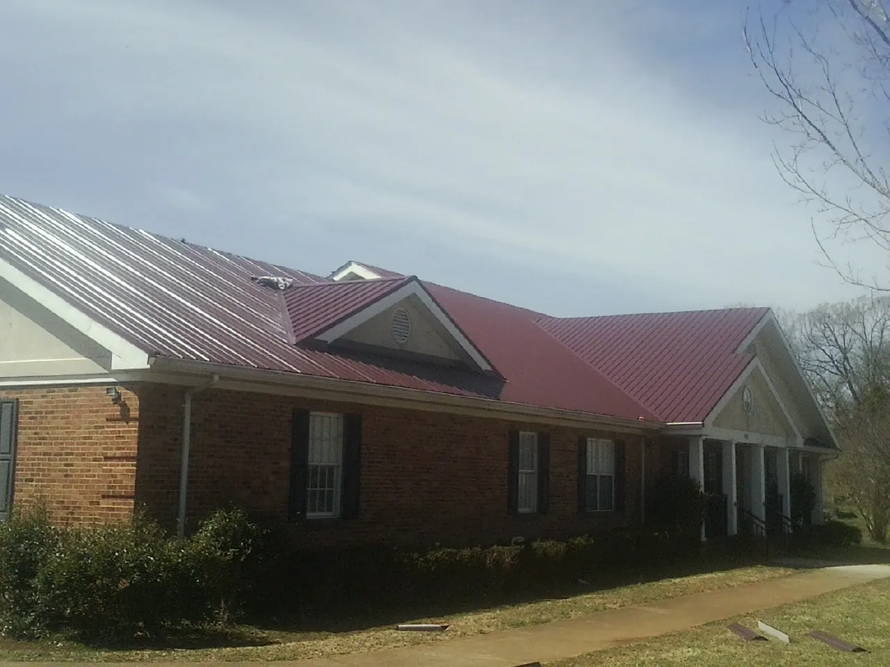 Red metal roof with gabled entries on a long brick building, from a Hail Damage Roof Repair job in Rienzi