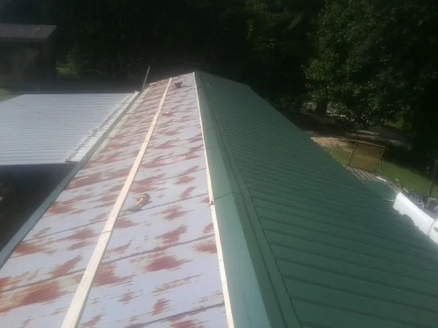 Old rusted panels beside newly installed green metal roofing — Wind Damage Roof Repair by Roofing Brothers in Rienzi