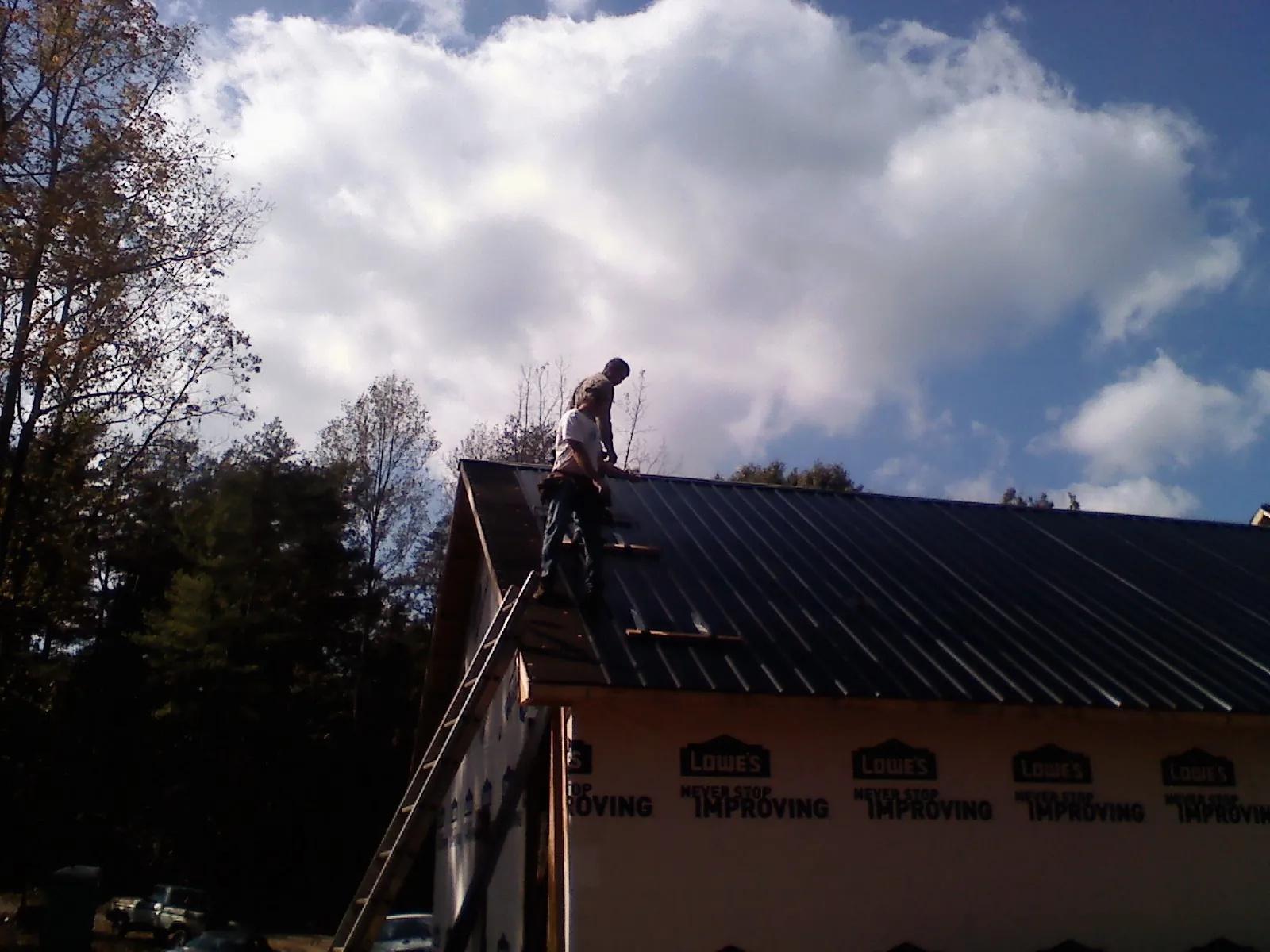 Roofer fastening dark metal panels high against a cloudy sky, from a Roof Inspection job in Rienzi