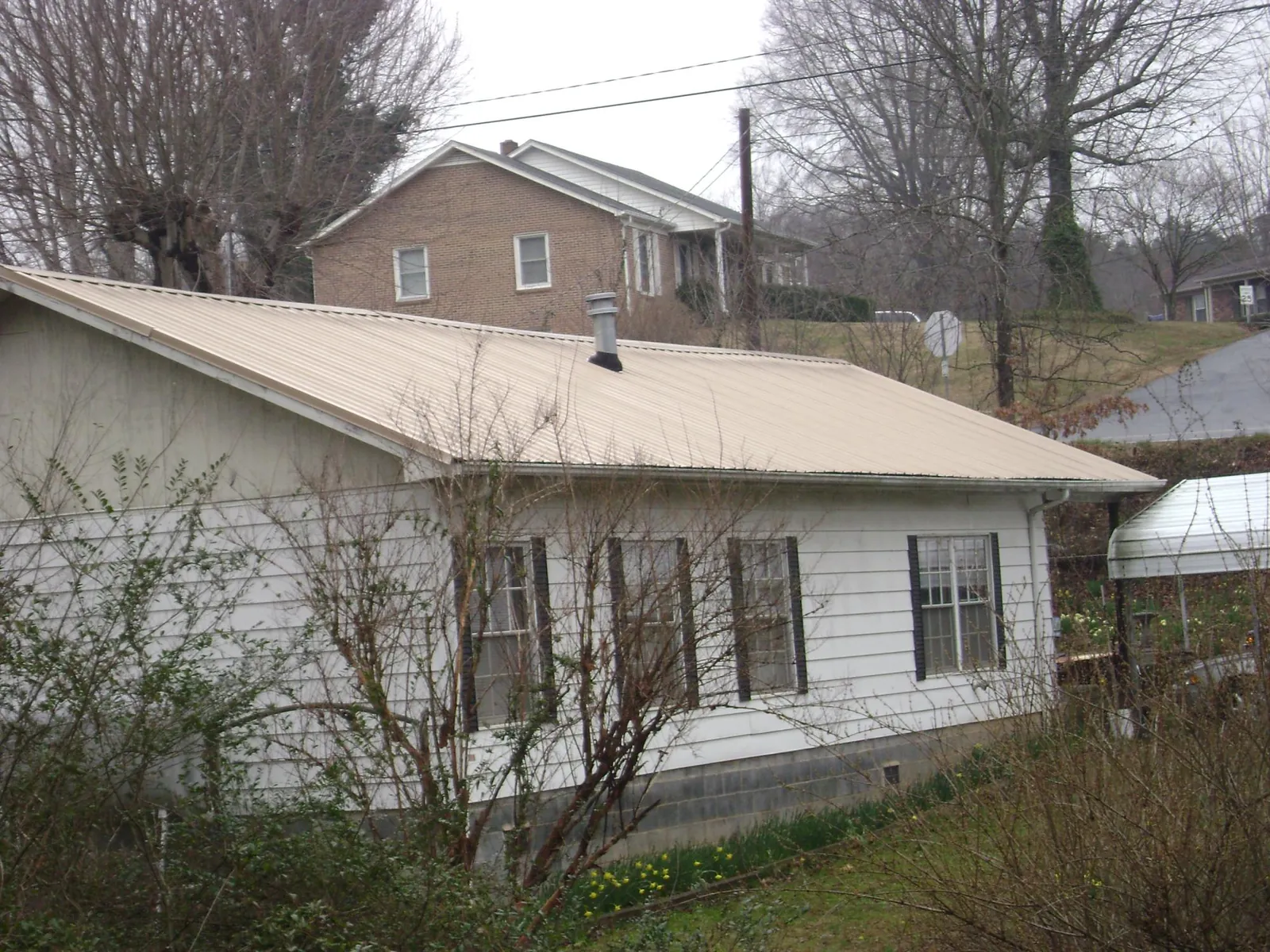 Tan metal roof on a white sided house set into a hillside — Commercial Roofing by Roofing Brothers in Rienzi