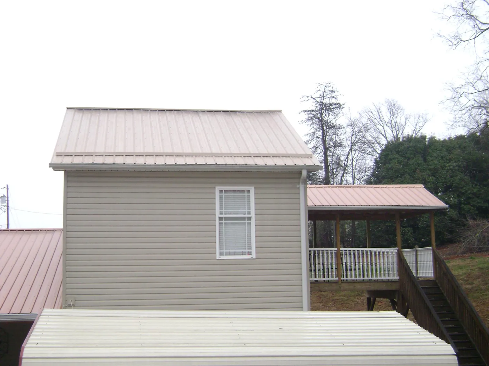 Tan metal roofs on a two story addition and attached porch, from a Roof Replacement job in Rienzi
